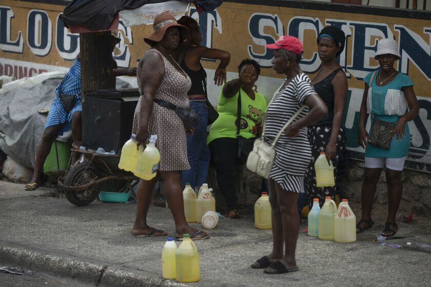 Women show their discomfort as they are being photographed selling contraband gasoline in plastic gallons jugs on a street in Port-au-Prince, Haiti, Thursday, July 14, 2022. (AP Photo/Odelyn Joseph)