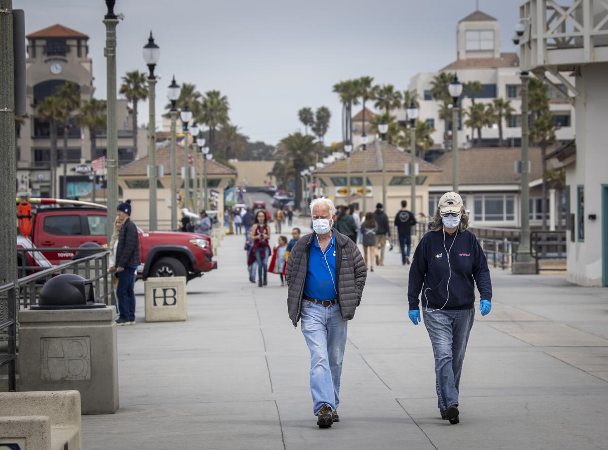 Dr. Dallas Weaver, and his wife, Janet Weaver, of Huntington Beach, wear their reusable protective masks and gloves that they will place in the oven and heat up to 160-degrees after their return from walking on the Huntington Beach pier amid coronavirus pandemic restrictions.