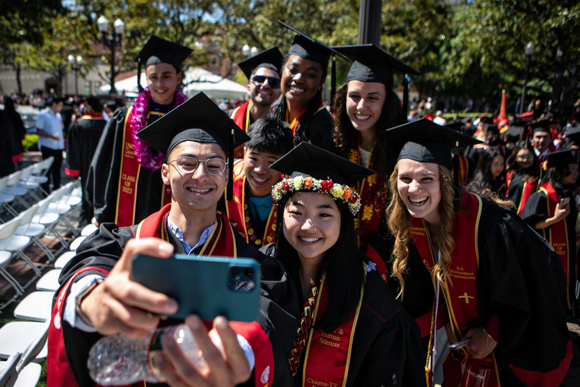 A group of grads smiles as one takes a selfie with his cellphone