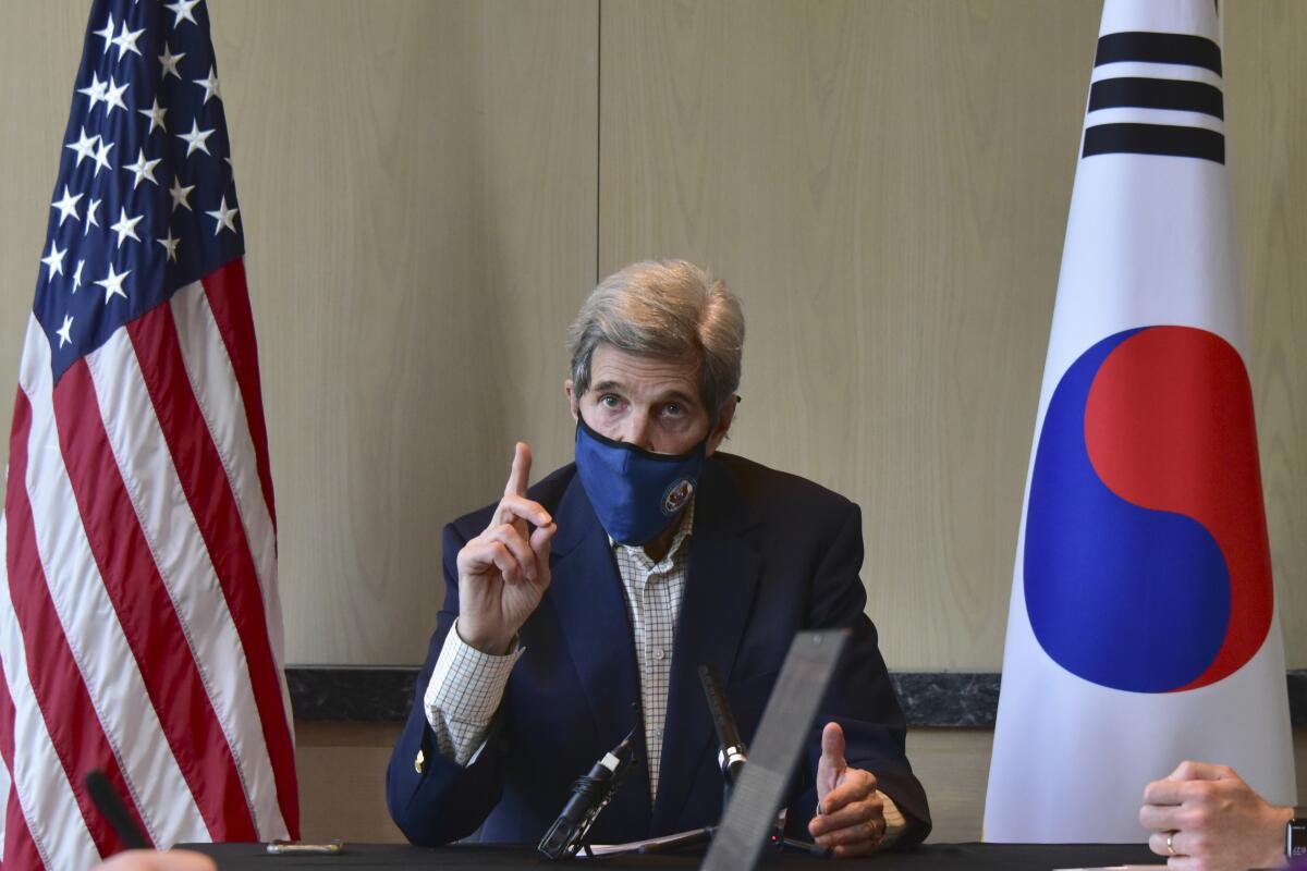 John Kerry raises his finger while sitting between a U.S. and South Korean flag.