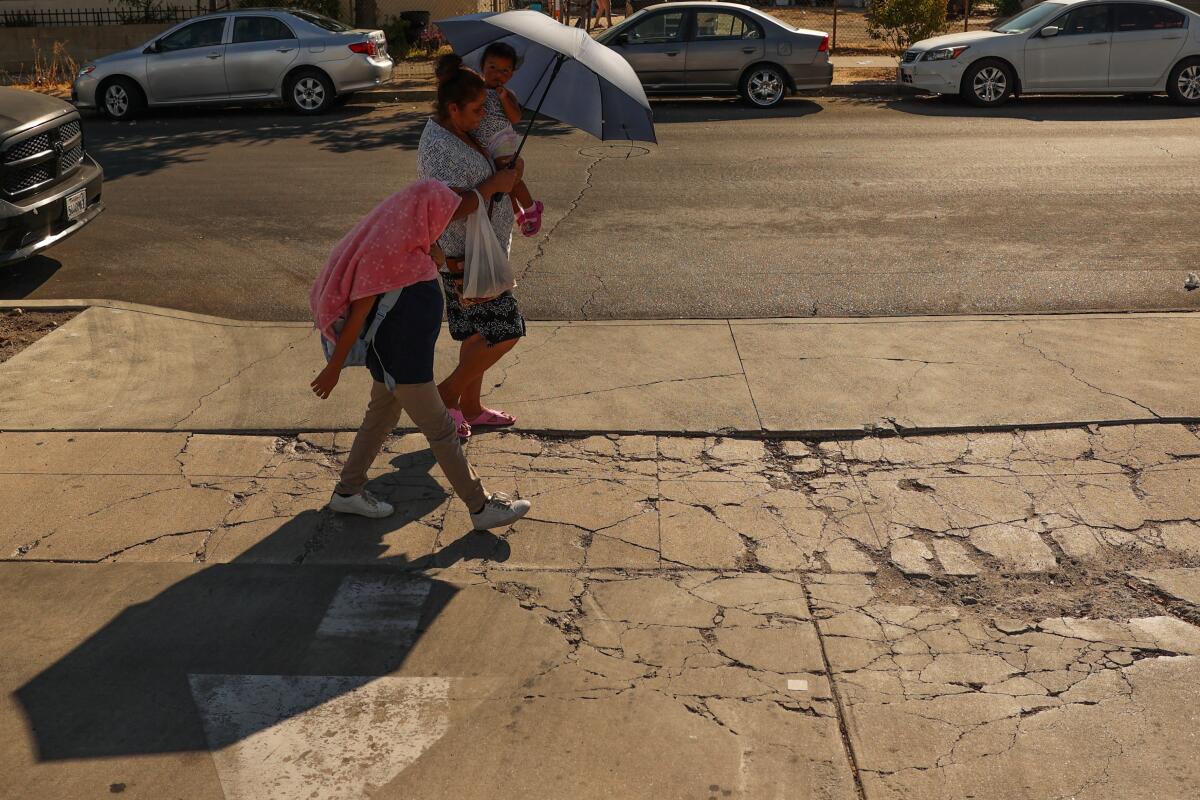 A family walks by while holding an umbrella and covering their head with a shirt on Friday, Sept. 6, 2024 in Pacoima, CA. 