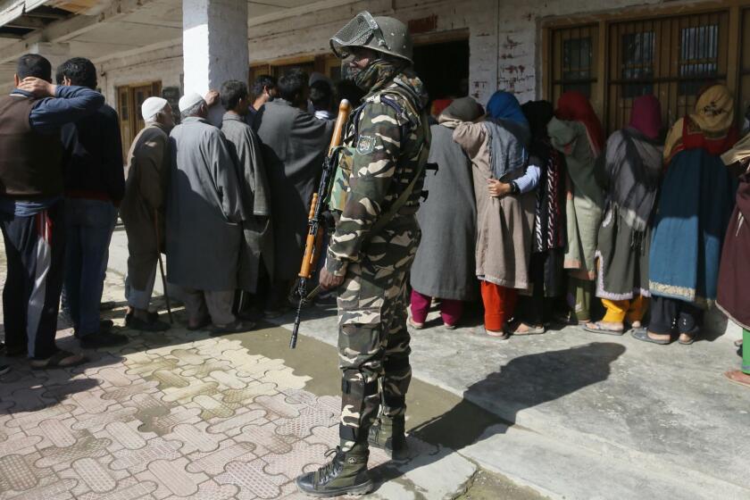 An Indian paramilitary soldier stands guard as Kashmiri voters wait in a queue to cast their votes outside a poling station during the second phase of India's general elections, on the outskirts of Srinagar, Indian controlled Kashmir, Thursday, April 18, 2019. Kashmiri separatist leaders who challenge India's sovereignty over the disputed region have called for a boycott of the vote. Most polling stations in Srinagar and Budgam areas of Kashmir looked deserted in the morning with more armed police, paramilitary soldiers and election staff present than voters. (AP Photo/Mukhtar Khan)