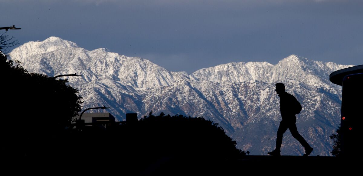 A pedestrian is silhouetted against snow-capped mountains.