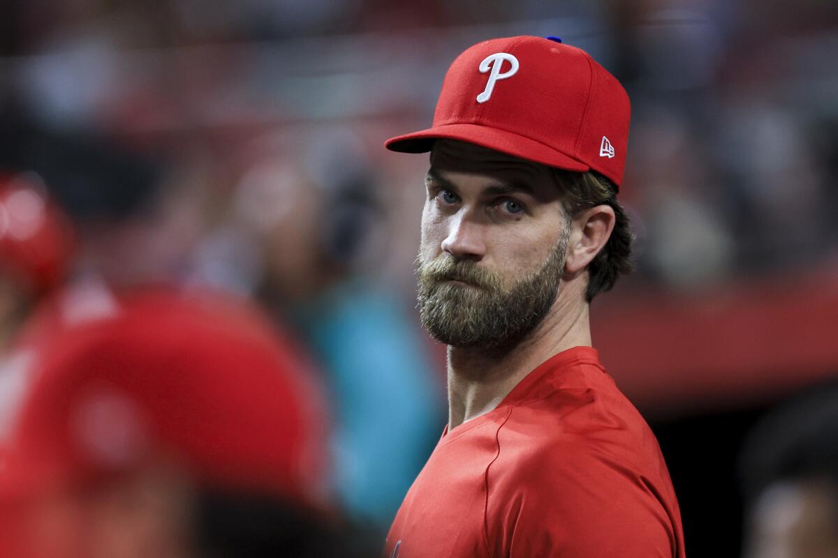 Philadelphia Phillies' Bryce Harper stands in the dugout during a baseball game.