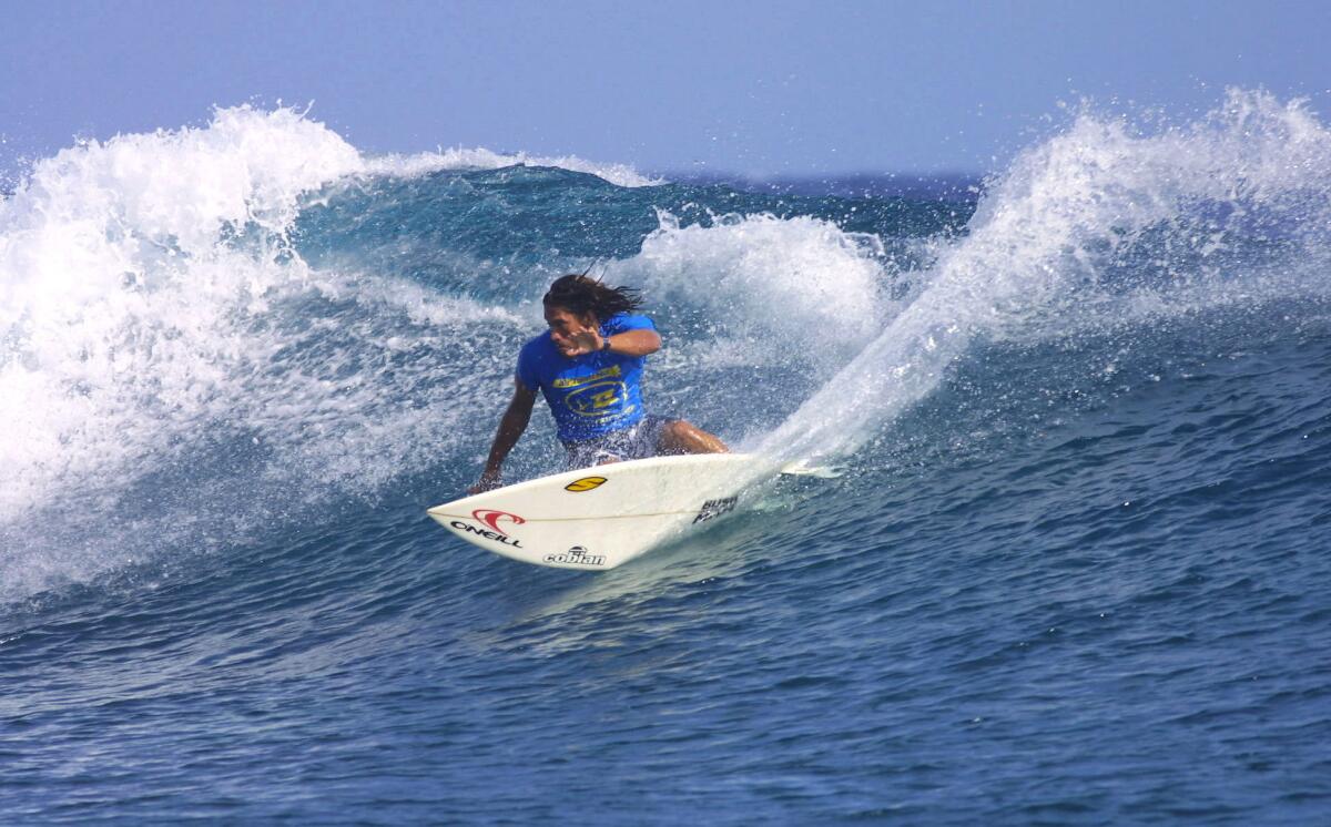 Tamayo Perry wearing a blue rashguard and surfing in Tahiti