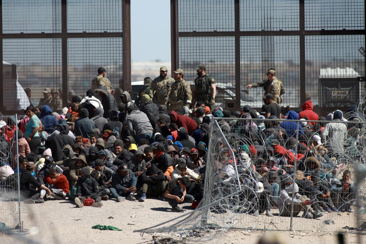 A crowd of migrants kneel as they wait to be processed at the border.