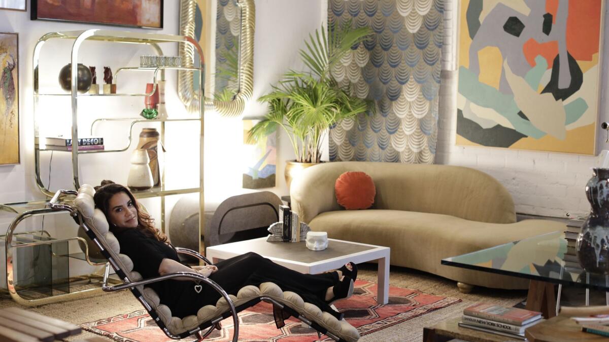A woman reclines on a lounge chair in an room filled with art and vintage furniture.