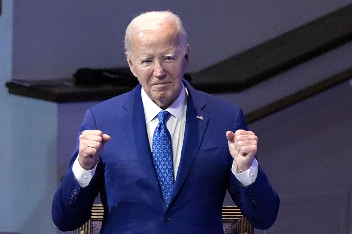 President Biden makes fists and holds them out in front of his blue suit jacket.