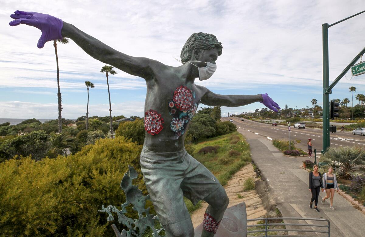 Rubber gloves, a mask, and what appears to be laboratory specimen depictions of the coronavirus are seen Wednesday on the Cardiff Kook statue in Encinitas.
