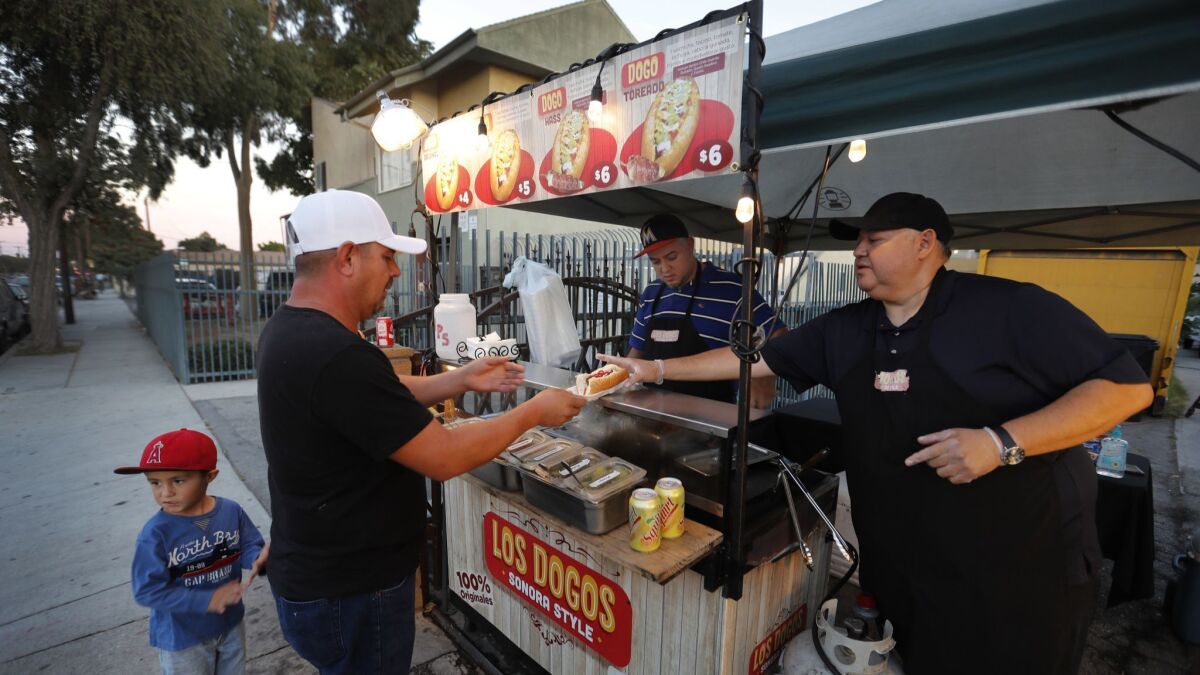 Alejandro Zamorano and his nephew David Zamorano serve Sonoran-style hot dogs at their cart in front of a friend's house in Compton