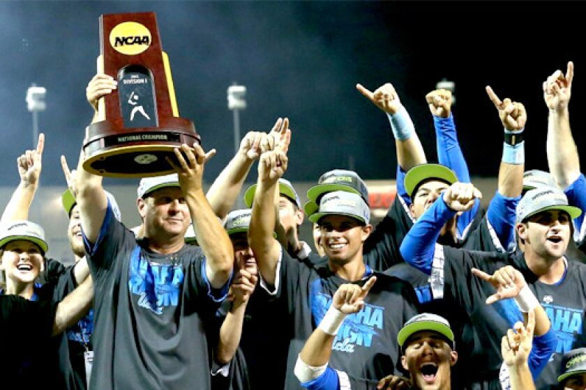 UCLA Coach John Savage, left, holds the Bruins' first baseball championship trophy after defeating Mississippi State, 8-0, to win the College World Series.