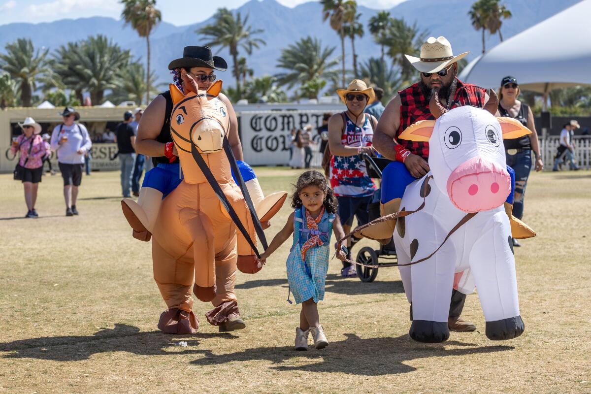 Two adults wearing inflatable horse and cow costumes walk with a child.