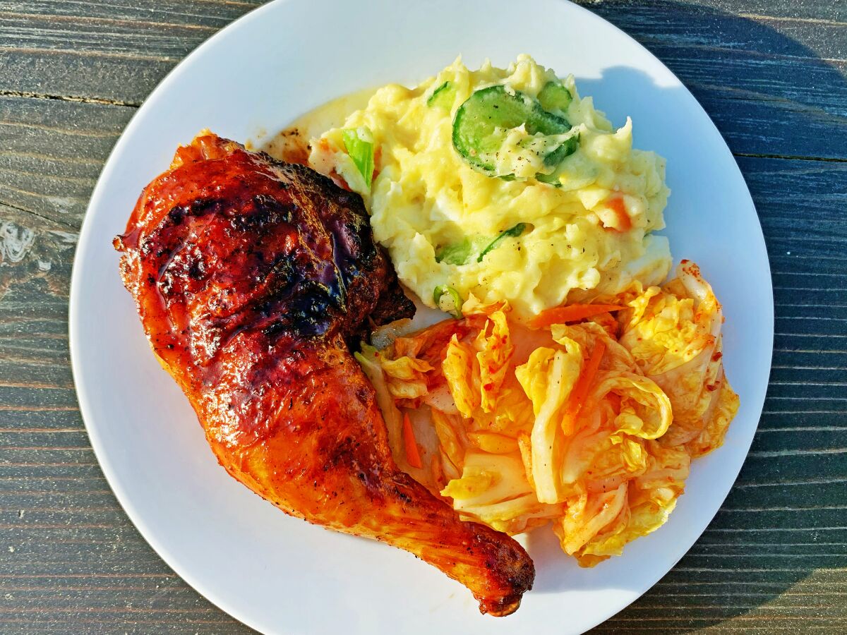 A plate of gochujang-glazed chicken with potato salad and kimchi.