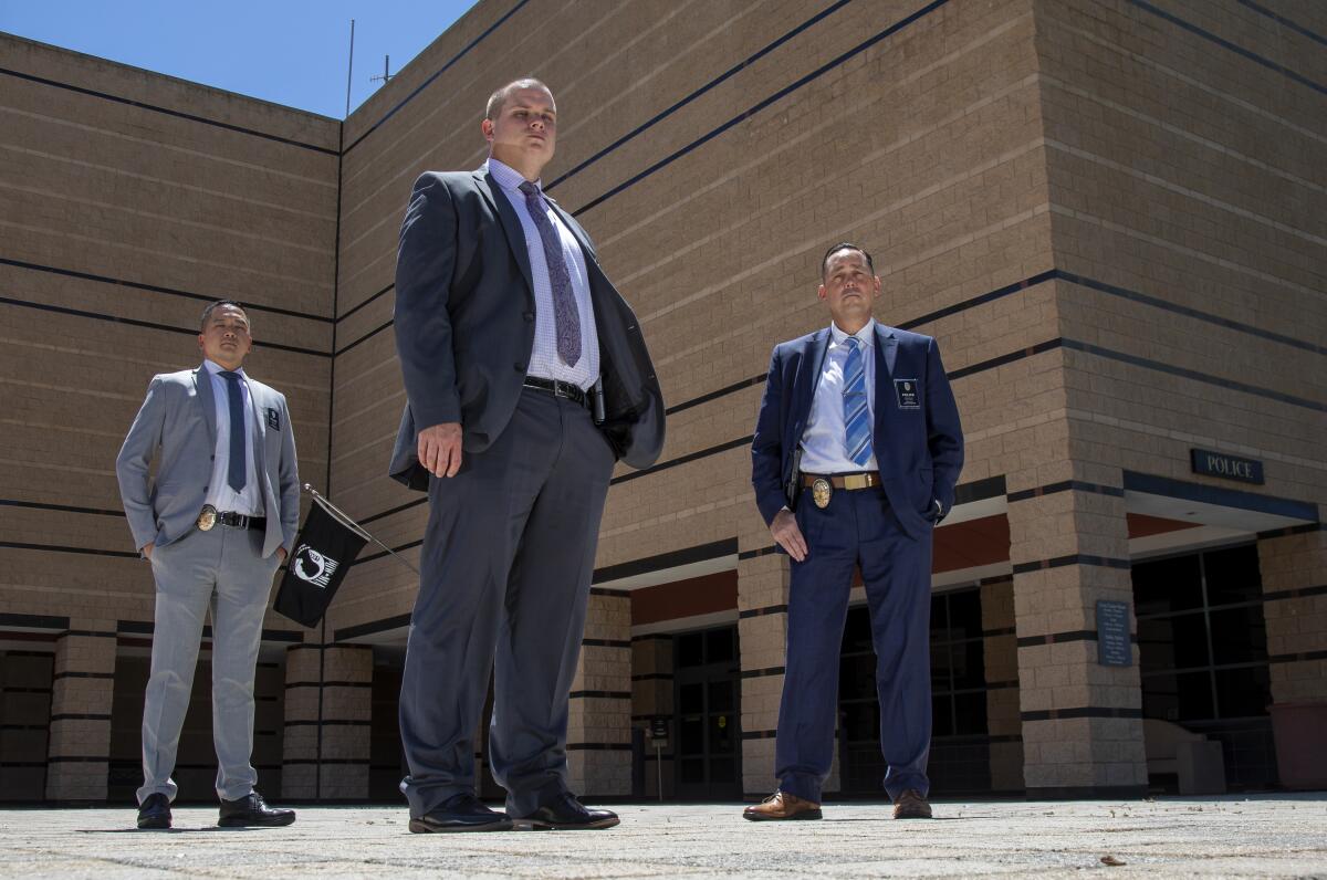 Three men in suits and ties, with badges on their belts, pose for a photo in front of a building.