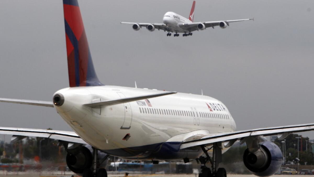 A Qantas A380 Airbus descends for landing while a Delta jet holds on the runway at Los Angeles International Airport. Delta Air Lines has eliminated a fee for booking flights by phone and at the ticket counters at U.S. airports.