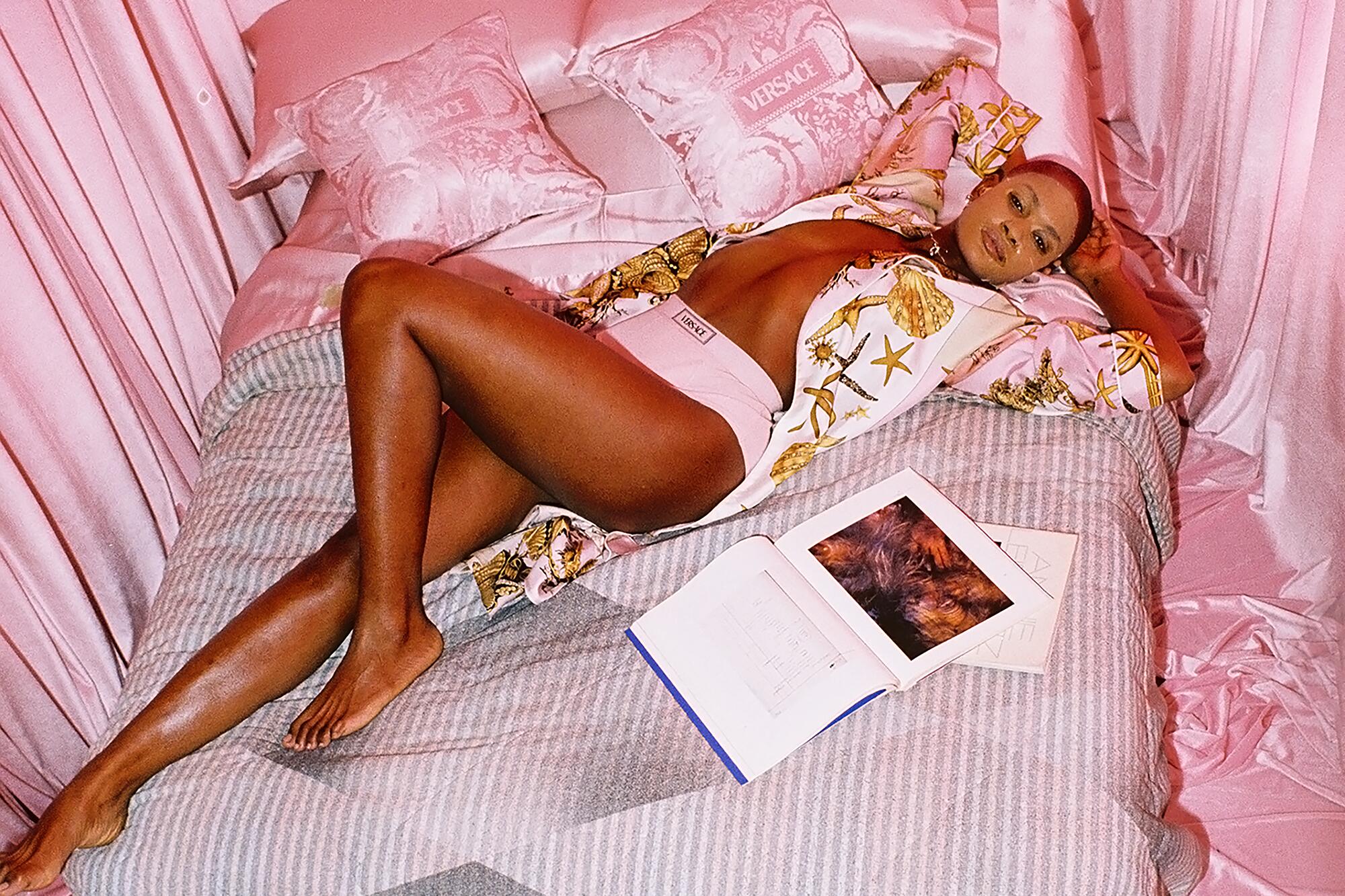 Pamela wears Versace briefs and robe, Justine Clenquet earrings and necklace, face mask. Versace <QL>bedding