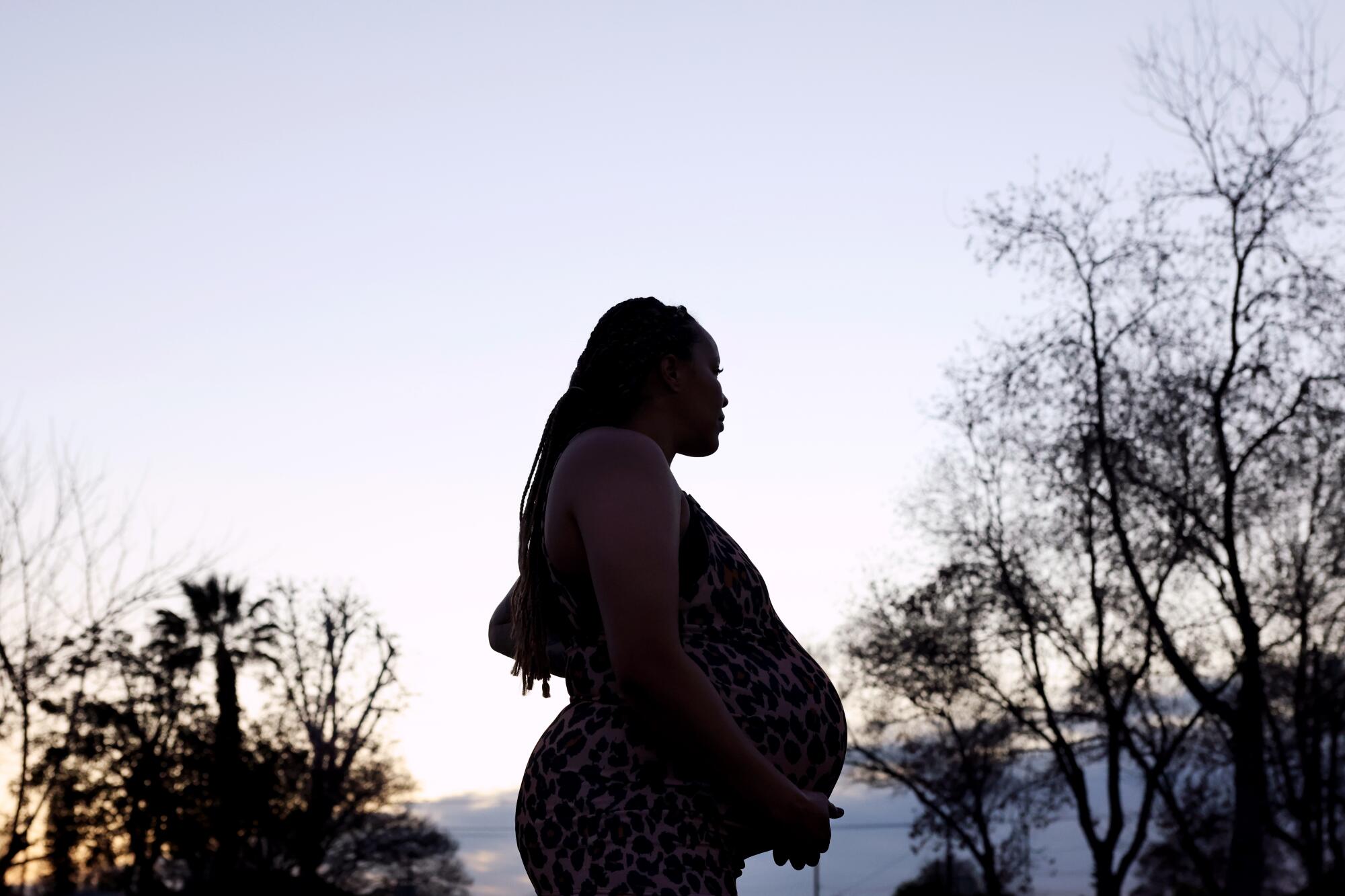 A pregnant woman shown in profile walks near trees.