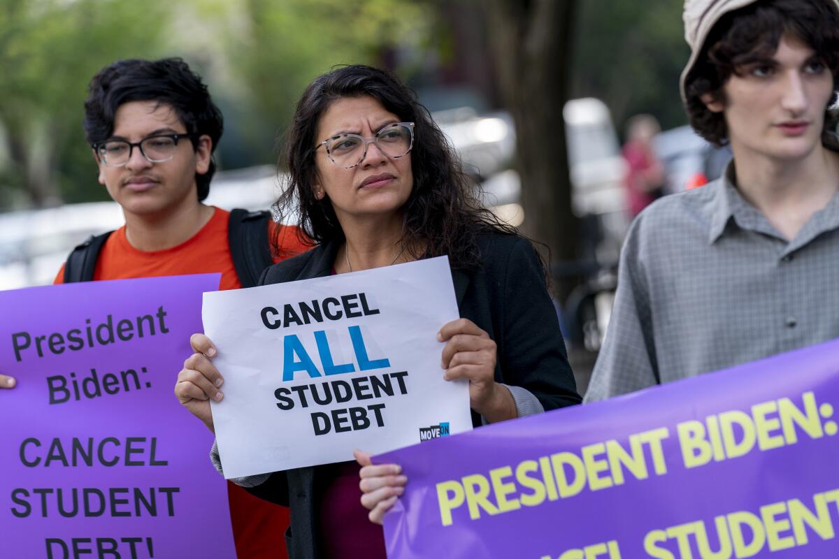Three people hold signs urging Biden to cancel student debt. 
