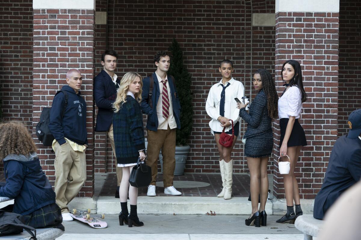 Seven teenagers in school uniforms stand on a school patio