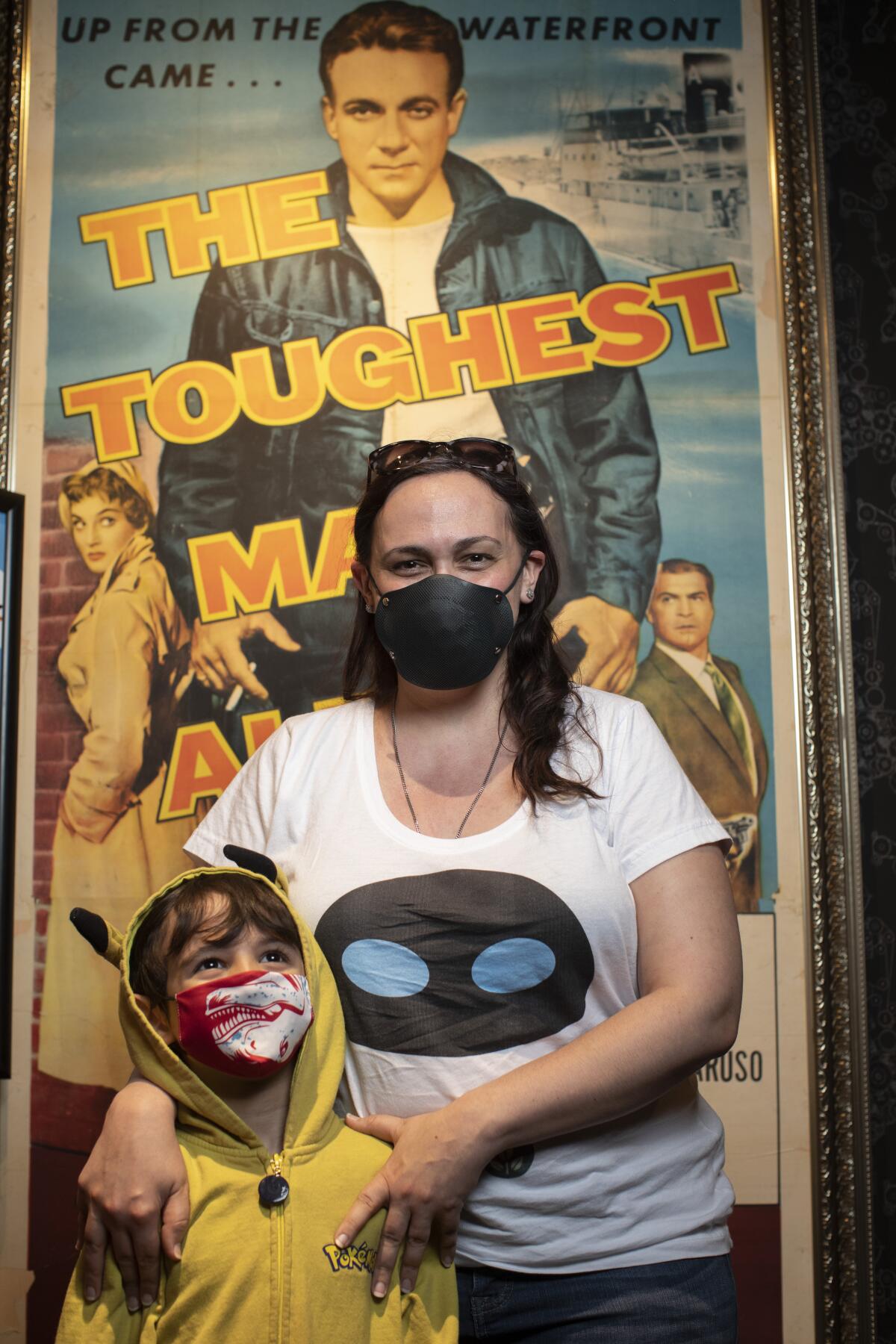 A woman and a young boy in a yellow hoodie stand in front of a movie poster.