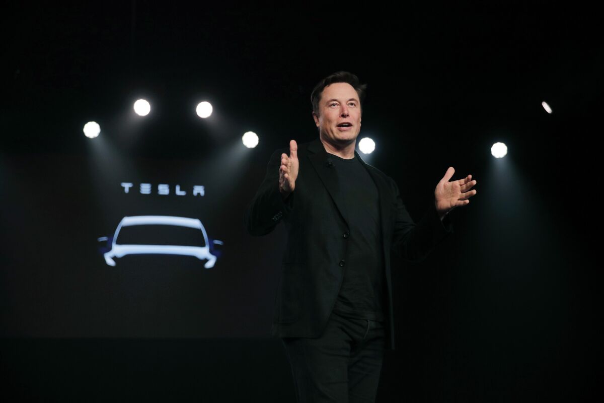 Tesla Chief Executive Elon Musk stands in front of a car with stage lights in the background.