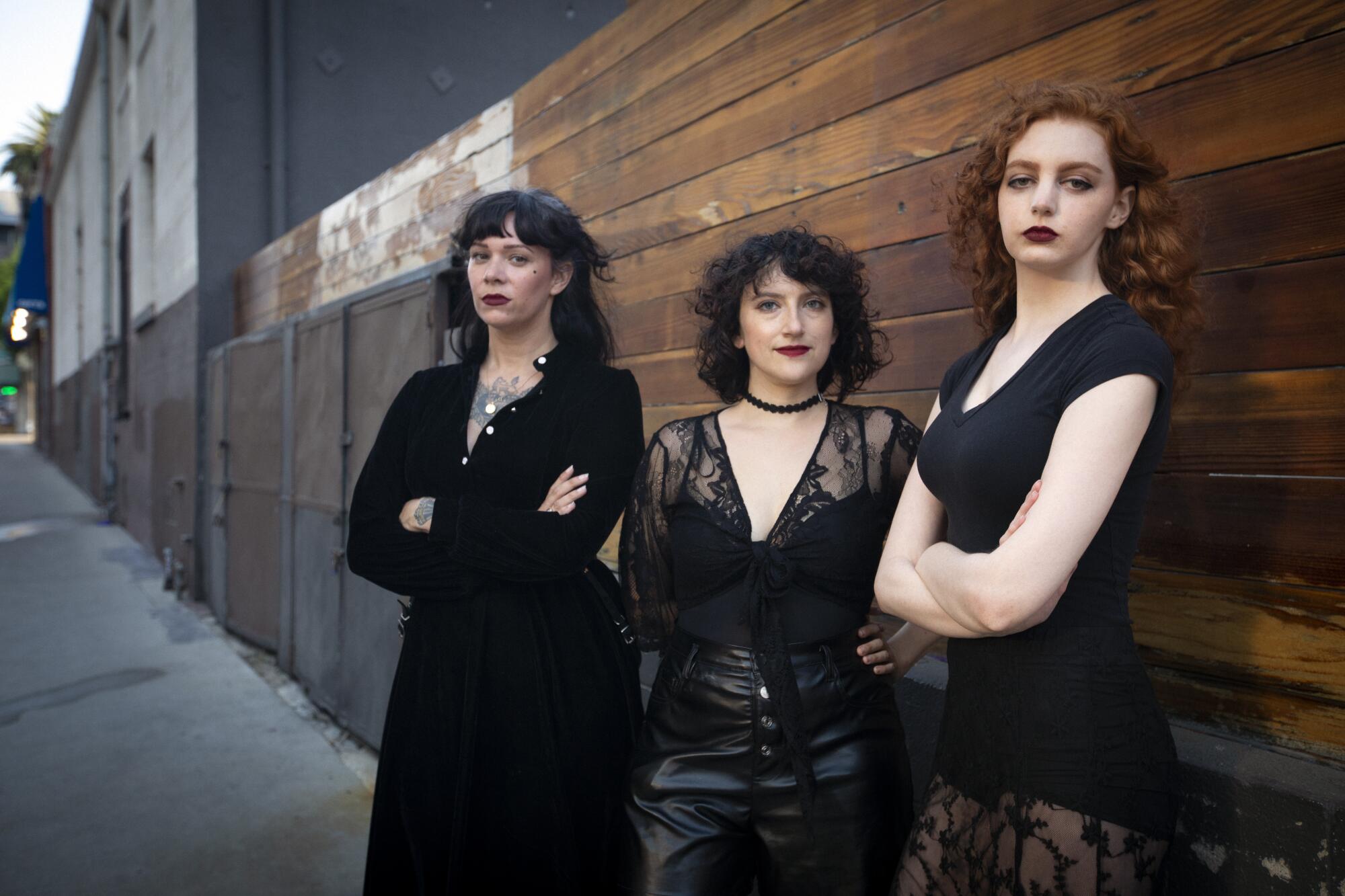 Kate Morgan, Annie Lesser and Alison Waxman stand on the sidewalk in front of a wooden fence. 