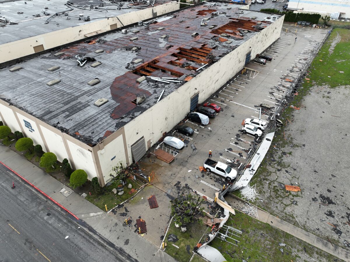 Portions of a building's roof is missing and an adjacent parking lot is littered with debris.