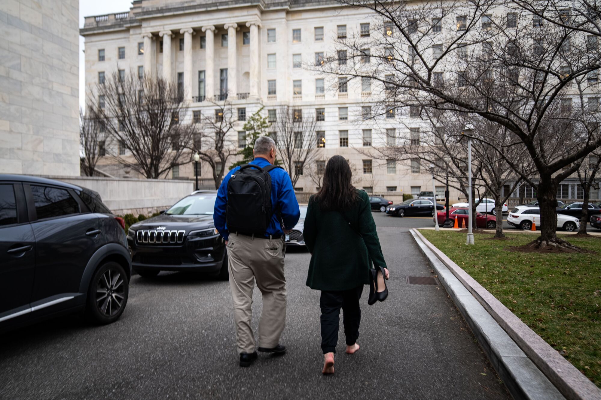 A man and woman walk past parked cars toward an office building.