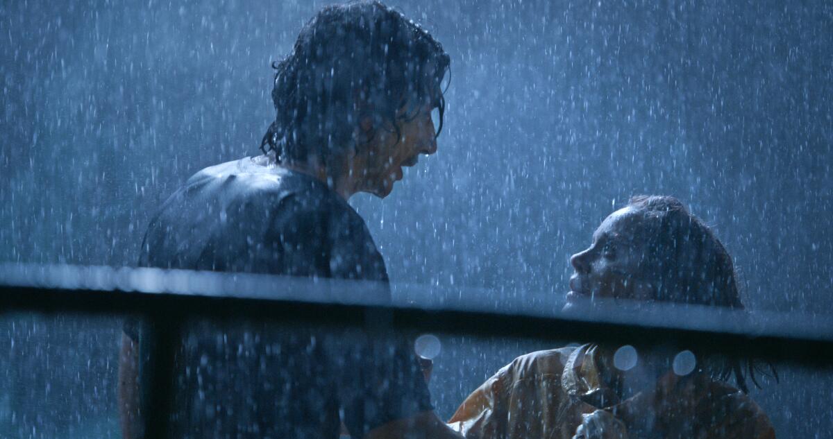 A man and a woman stand talking in the driving rain.