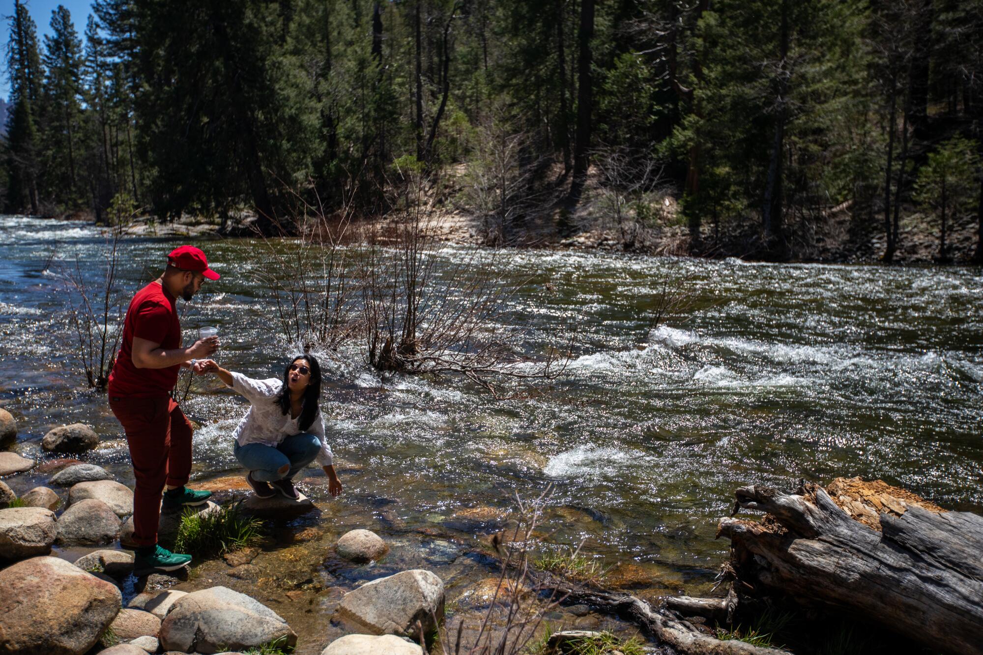A woman reaches down to touch Merced River in Yosemite.