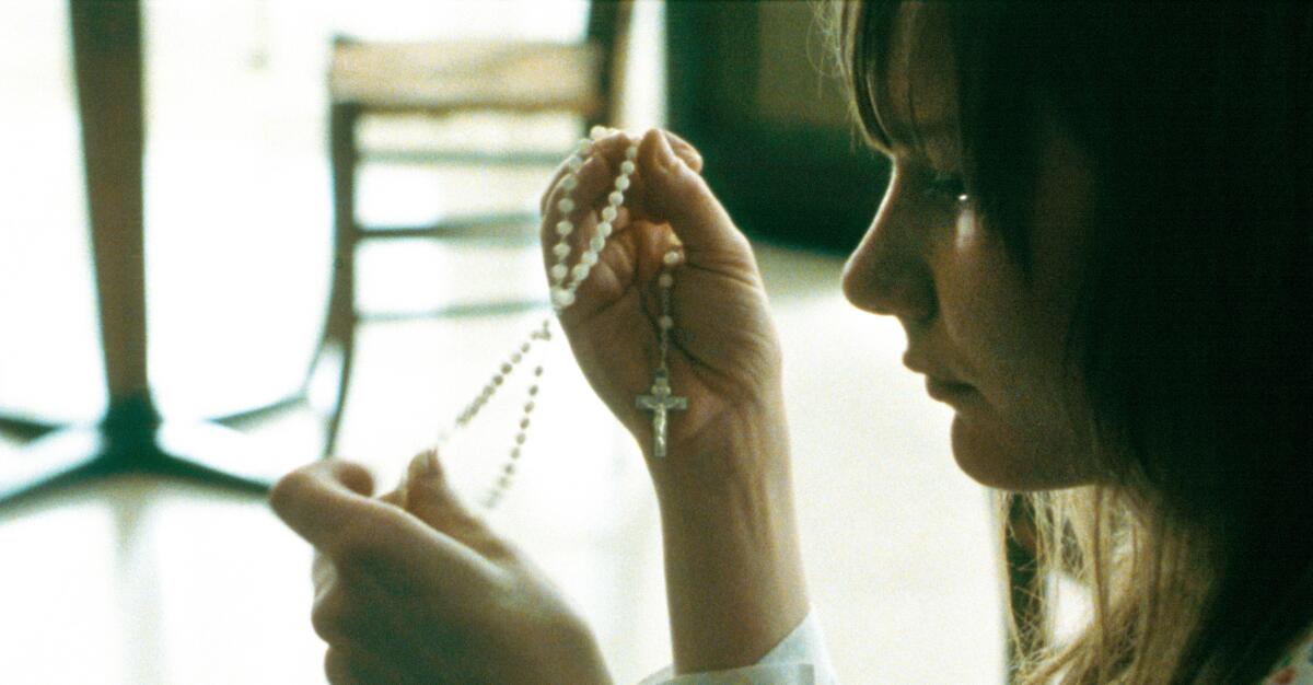 A woman holds rosary beads in her hands.