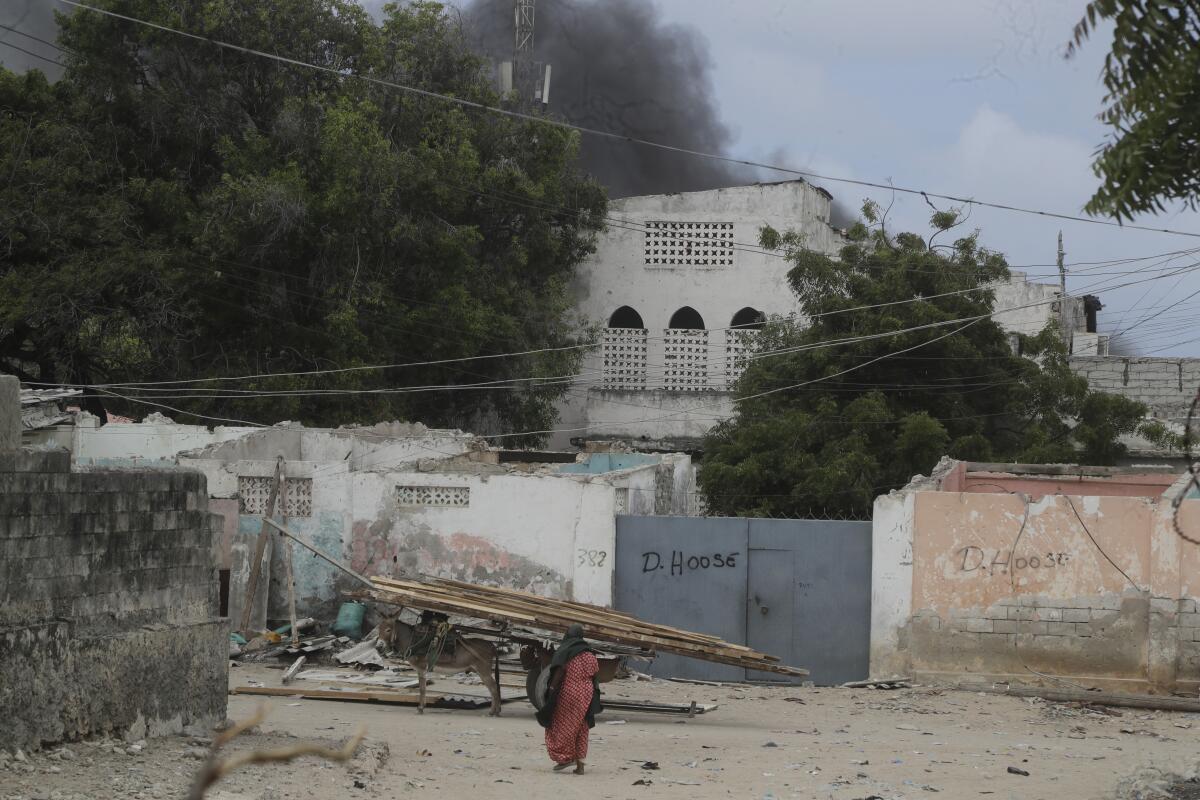 A woman walks on a beach as black smoke is seen rising in the background in Mogadishu, Somalia.