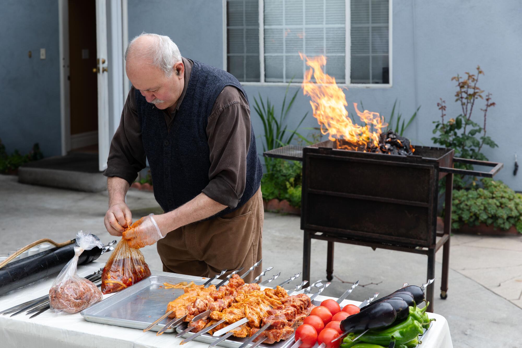 Alex Khachoyan prepares meat for grilling with a flaming grill behind him in his backyard.