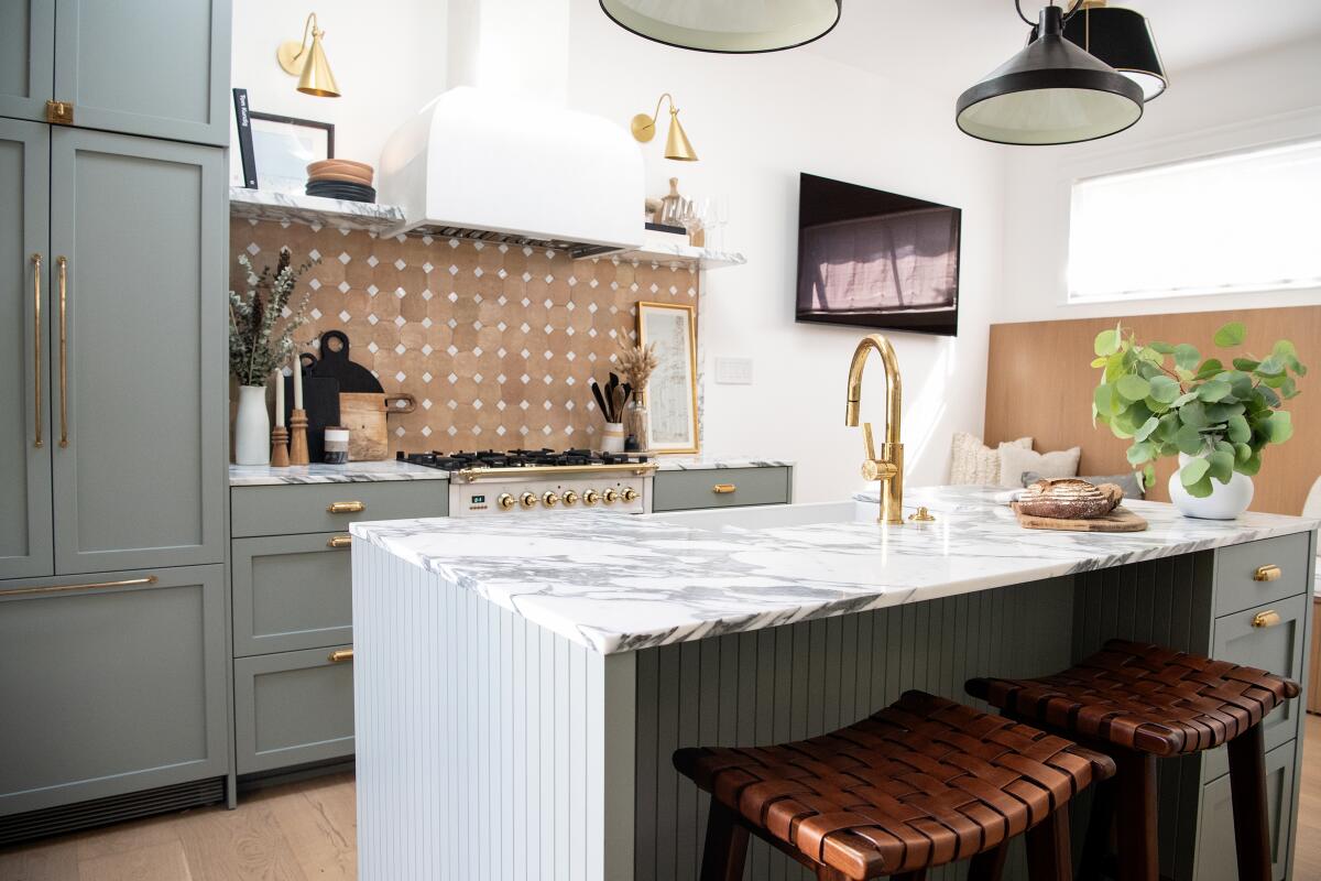 Two barstools tuck under a kitchen countertop bar, which also features a sink with a gold faucet.