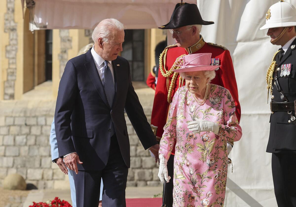Biden reaches out a hand to Queen Elizabeth, followed by British military men in uniform.