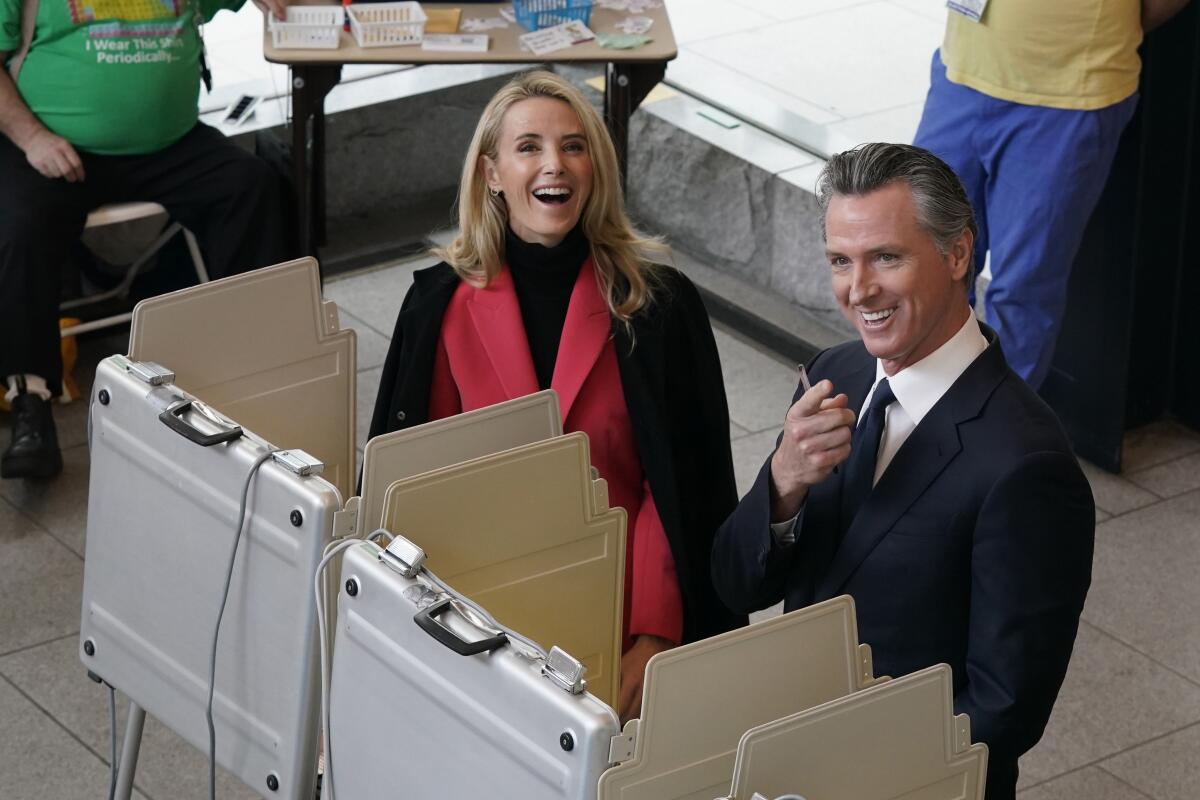 Gov. Gavin Newsom and his wife, Jennifer Siebel Newsom, laugh after they spot photographers watching them while voting.