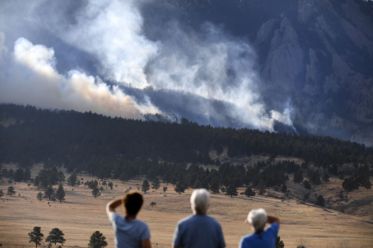 From left, Laura Tyson, Tod Smith and Rebecca Caldwell, residents of Eldorado Springs, watch as the NCAR fire burns in the foothills south of the National Center for Atmospheric Research, Saturday, March 26, 2022, in Boulder, Colo. The NCAR fire prompted evacuations in south Boulder and pre-evacuation warning for Eldorado Springs. According to a study published in Science Advances on Friday, April 1, 2022, a one-two punch of nasty wildfires followed by heavy downpours, triggering flooding and mudslides, will strike the U.S. West far more often in a warming-hopped world, becoming a frequent occurrence. (Helen H. Richardson/The Denver Post via AP, File)
