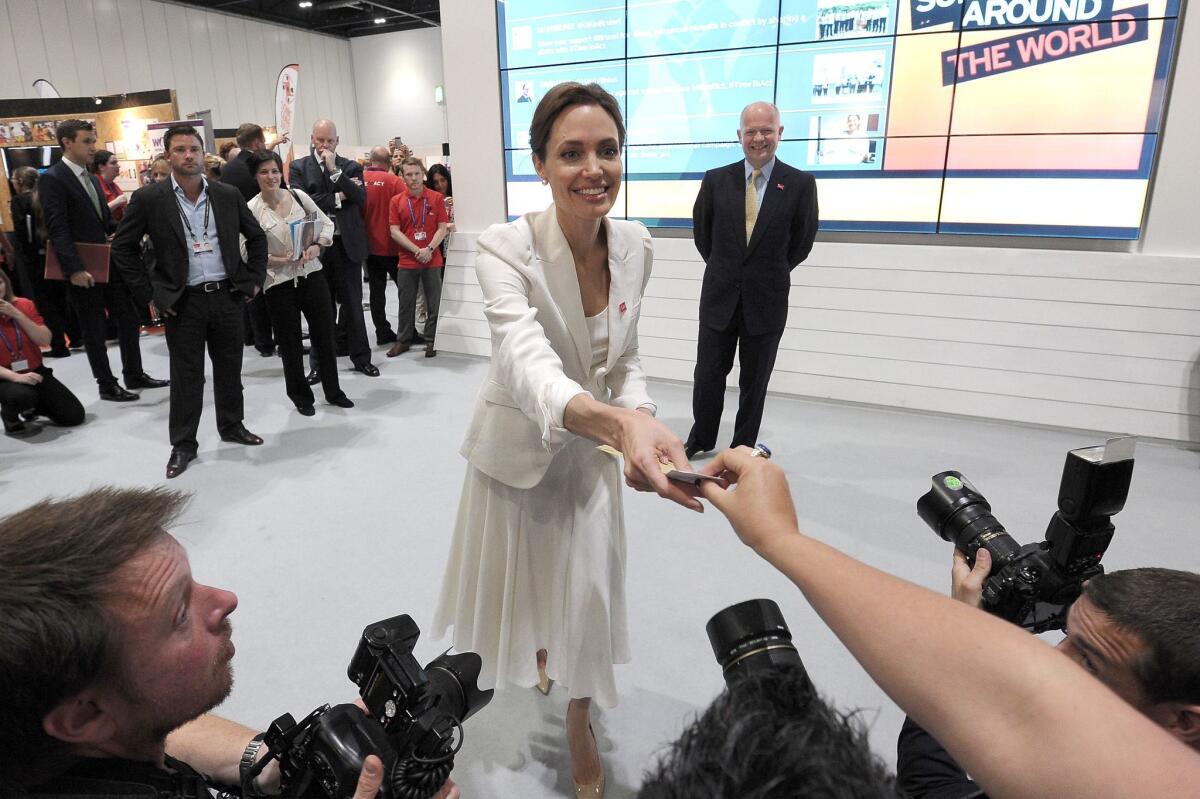 Angelina Jolie receives a note from a visitor as she and British Foreign Secretary William Hague, right, visit exhibitors during the first day of the Global Summit to End Sexual Violence in Conflict in London.