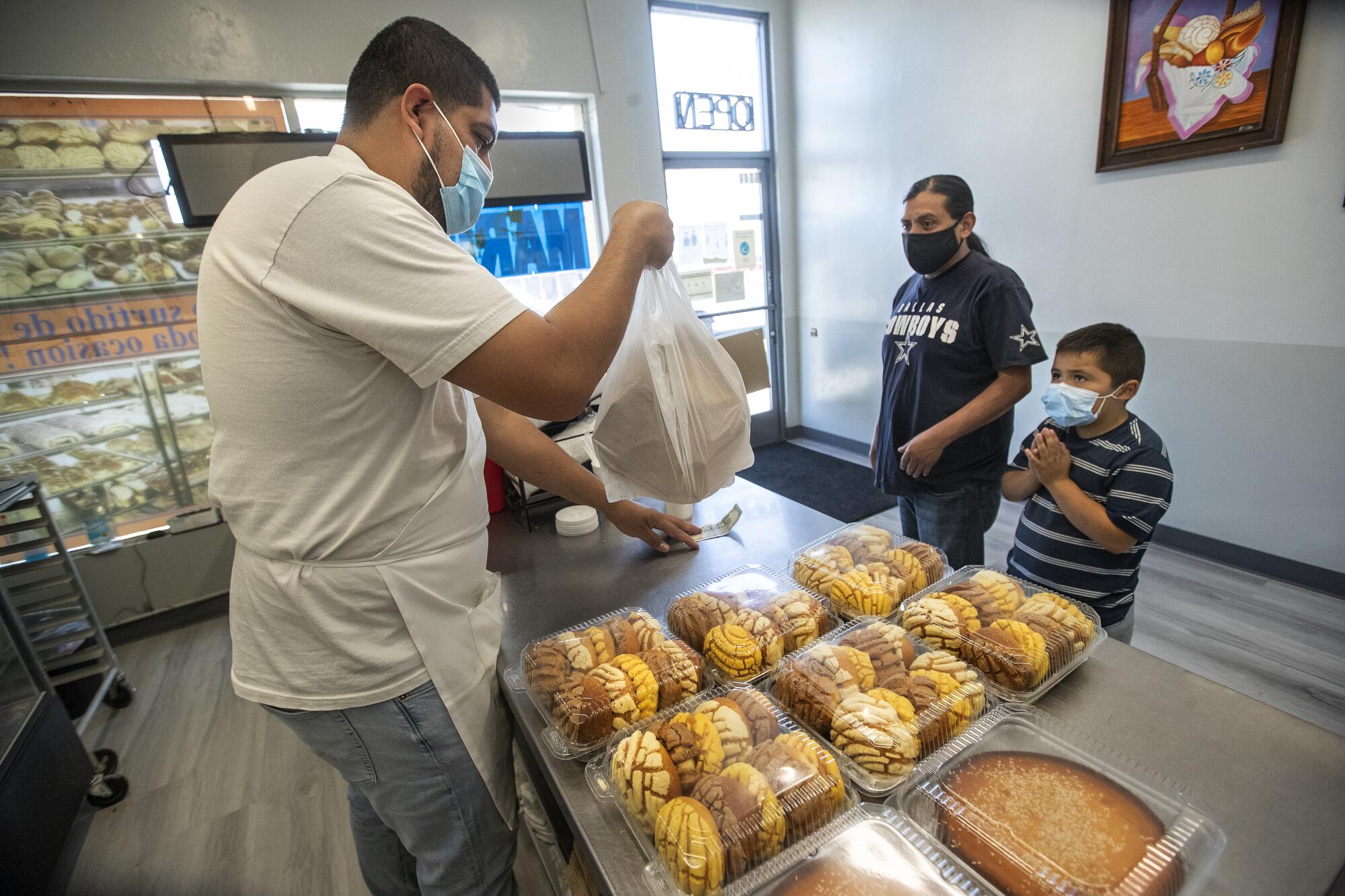 Jesse Dominguez prepares to hand a bag of fresh baked bolillos to customer Genaro Galindo, with his nephew, Dylan Arreola, 5.