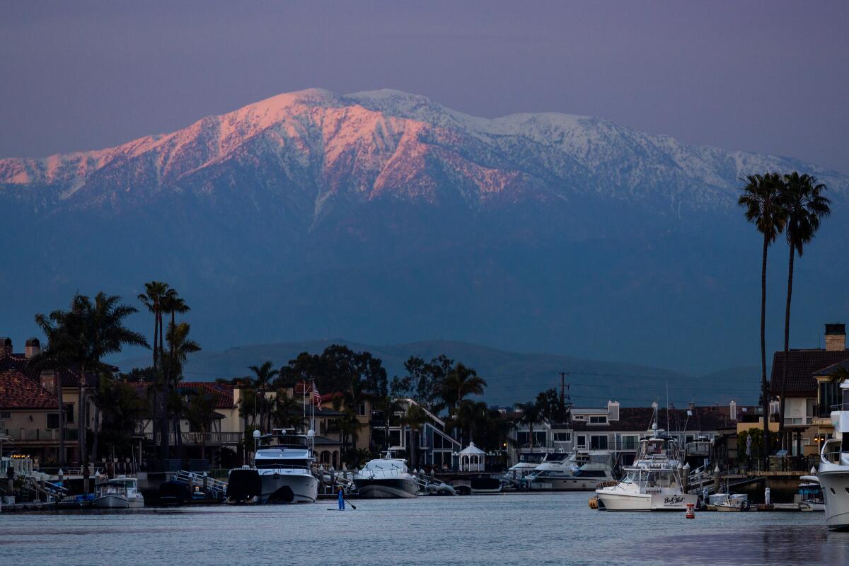 A stand-up paddle boarder cruises as the setting sun illuminates the top of the San Gabriel Mountains in Huntington Harbour