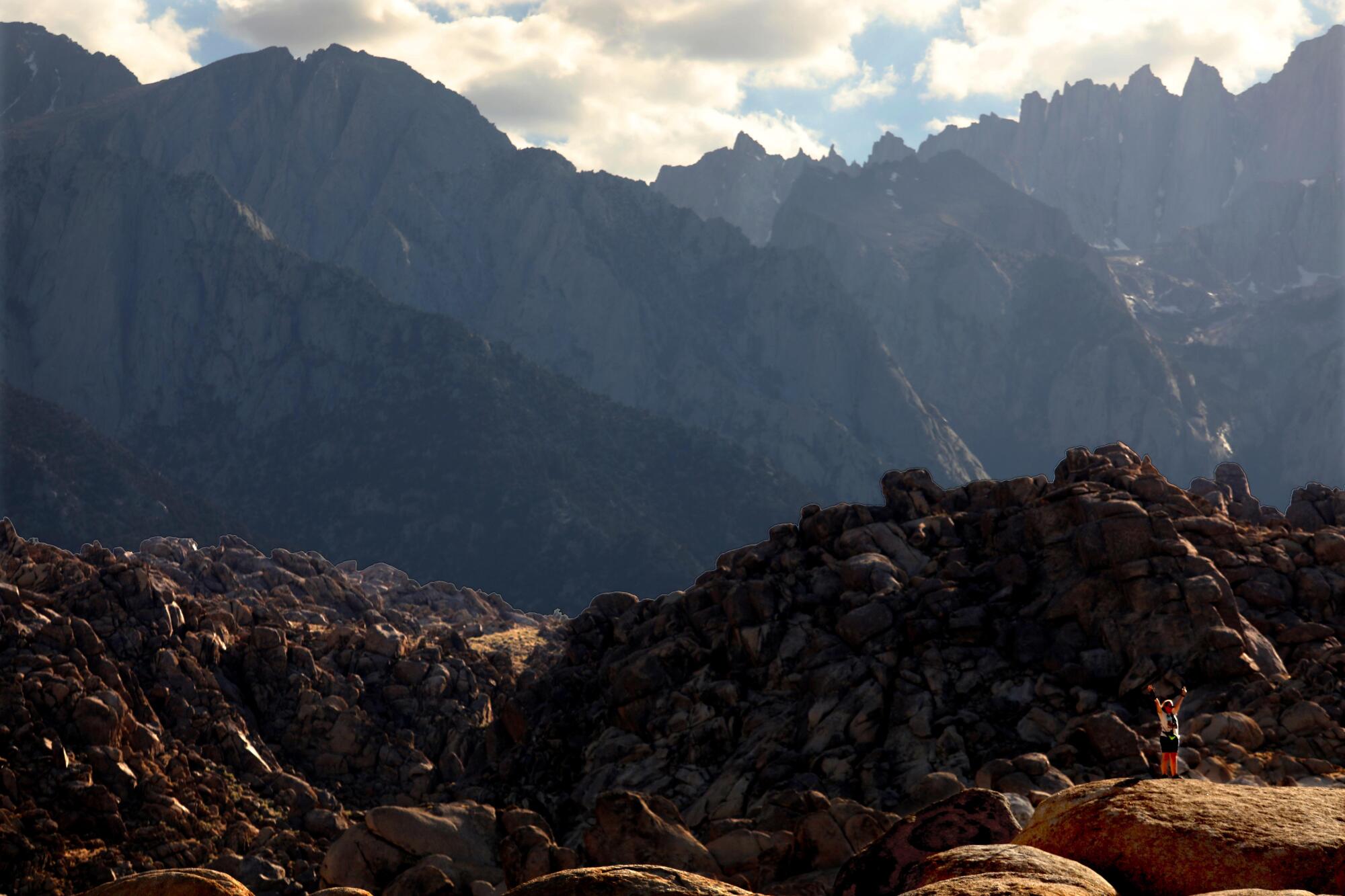 A woman poses with her arms raised for a photo against the backdrop of Alabama Hills National Scenic Area and Eastern Sierra