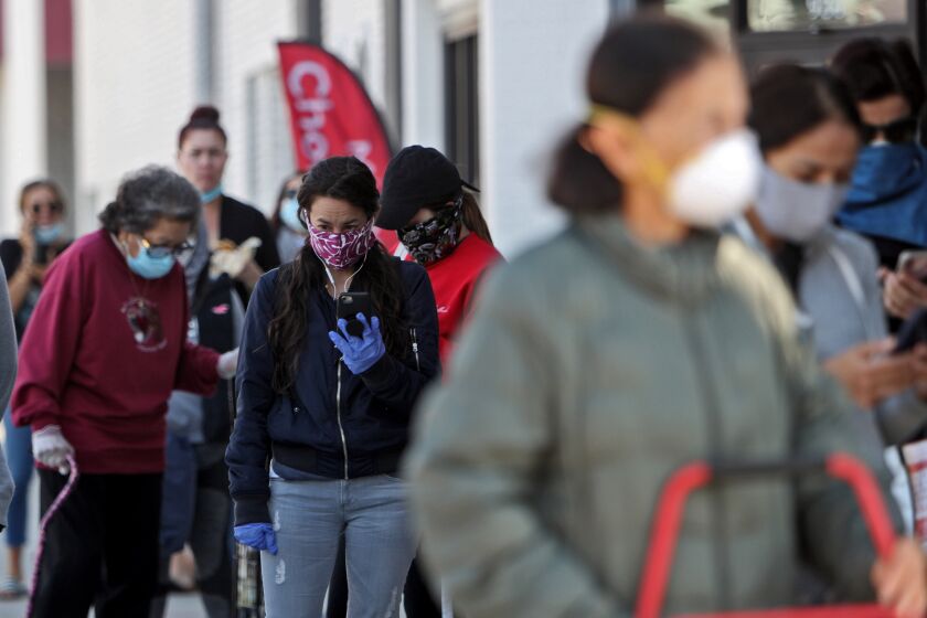 Customers waiting to enter, line up wearing face masks at Trader Joe's, on E. Glenoaks Blvd., in Glendale on Tuesday, April 14, 2020.
