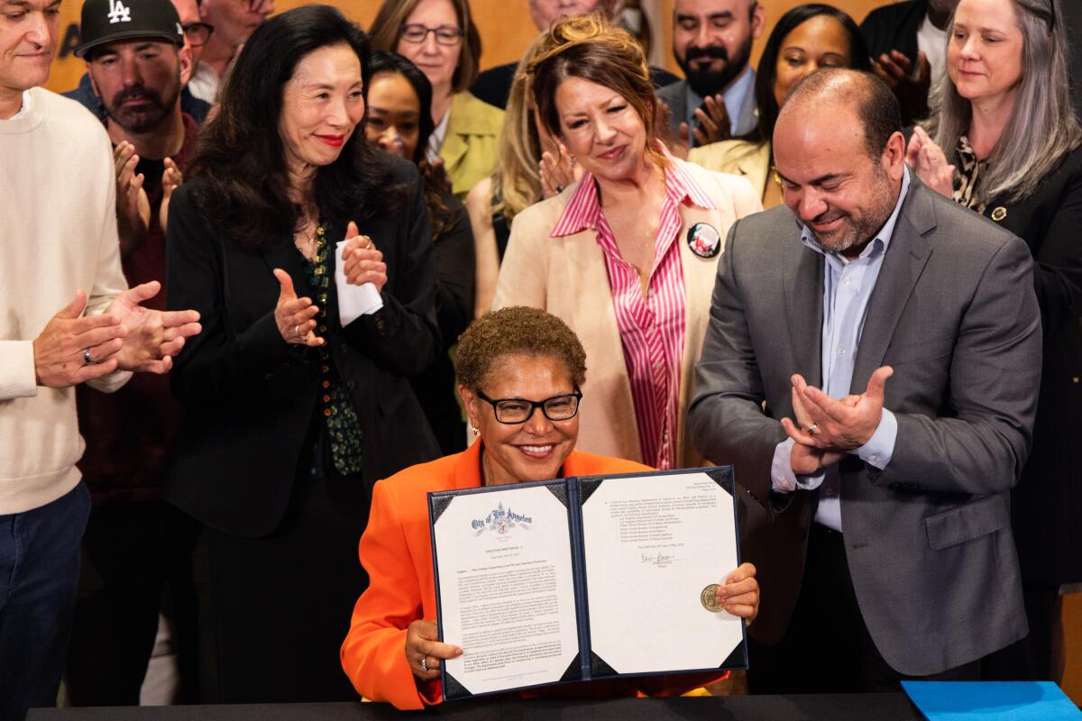 Mayor Karen Bass flanked by people holding the executive directive she just signed