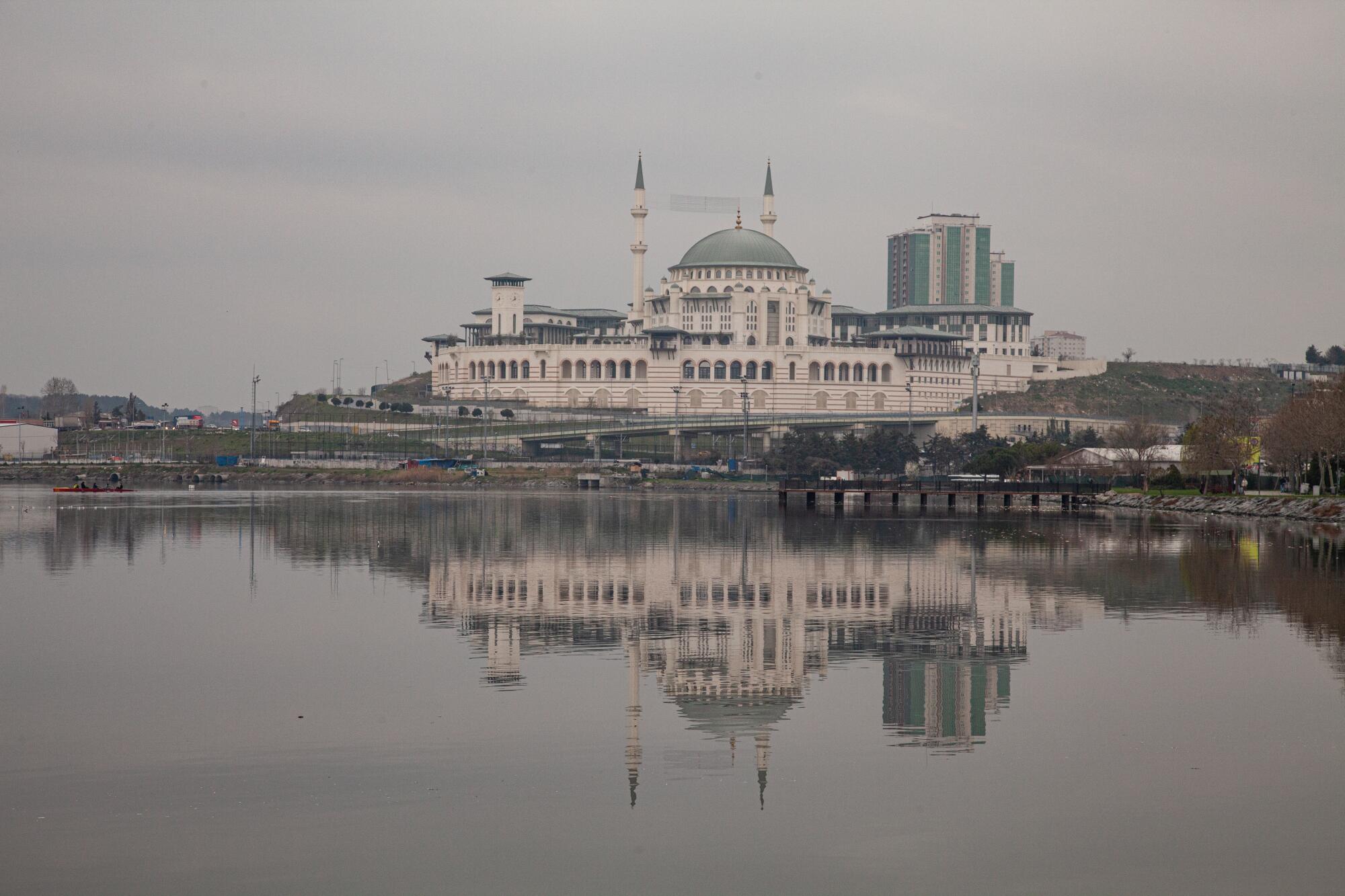 A view of a lake and a sprawling white building with a blue dome and minarets 