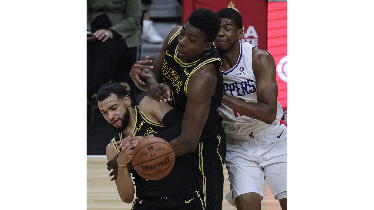Lakers guard Tyler Ennis and center Thomas Bryant struggle to control the ball as Clippers guard Tyrone Wallace pressures them during first half action.