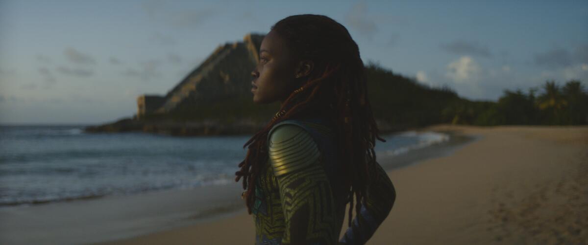 A woman in warrior attire stands on a beach.