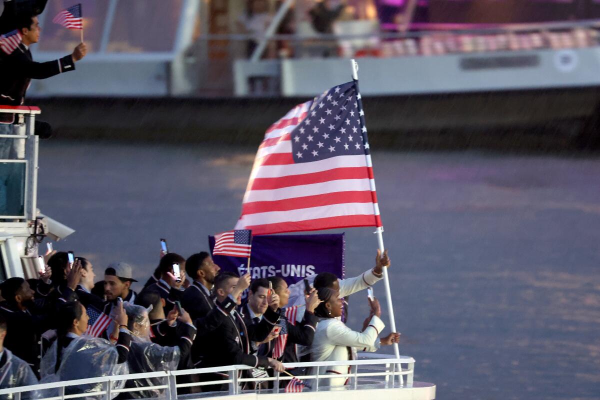 a woman and man holding up the U.S. flag at the front of a boat