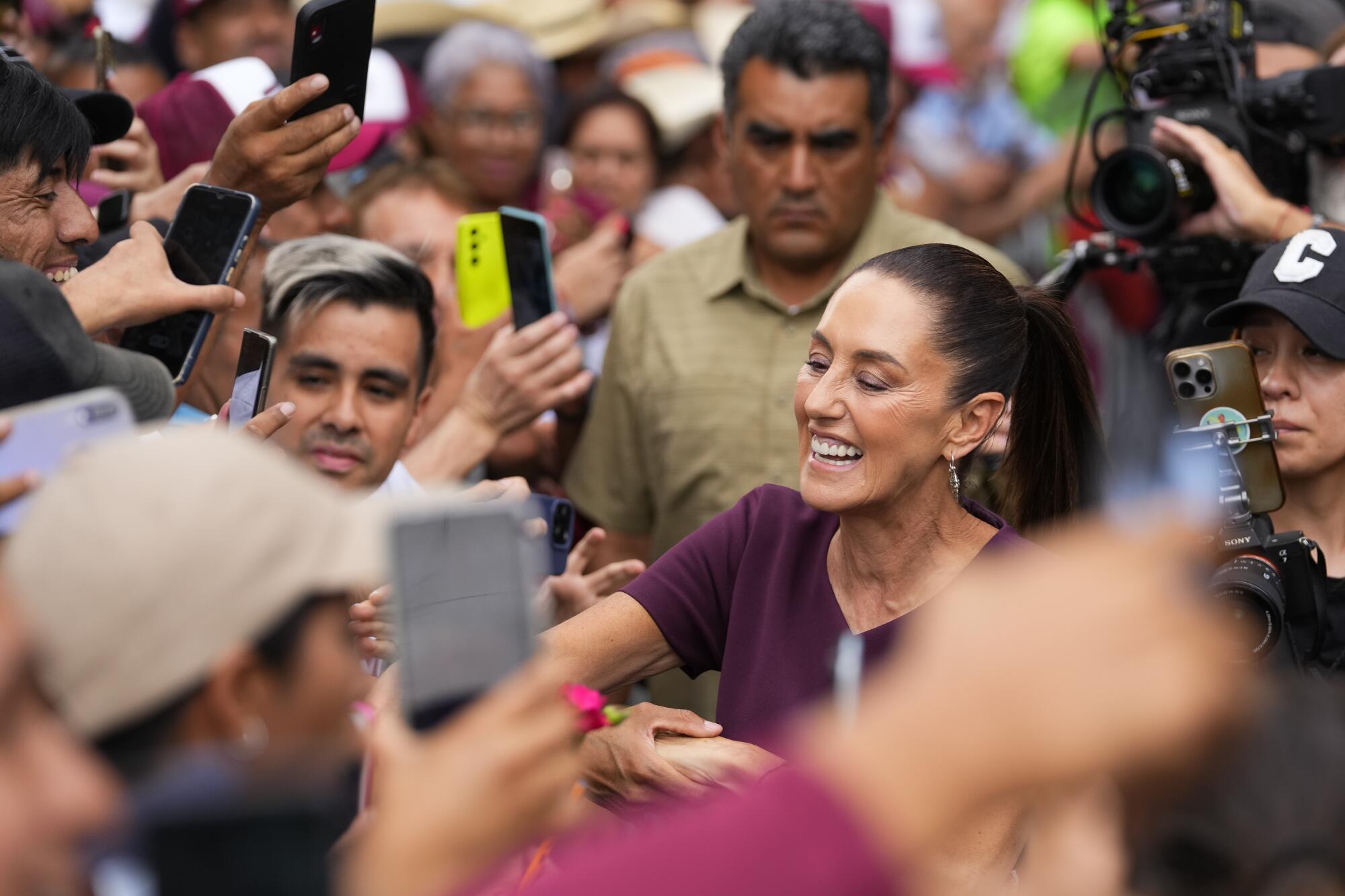 A woman with her hair pulled back in a ponytail smiles and reaches out to greet people surrounding her.