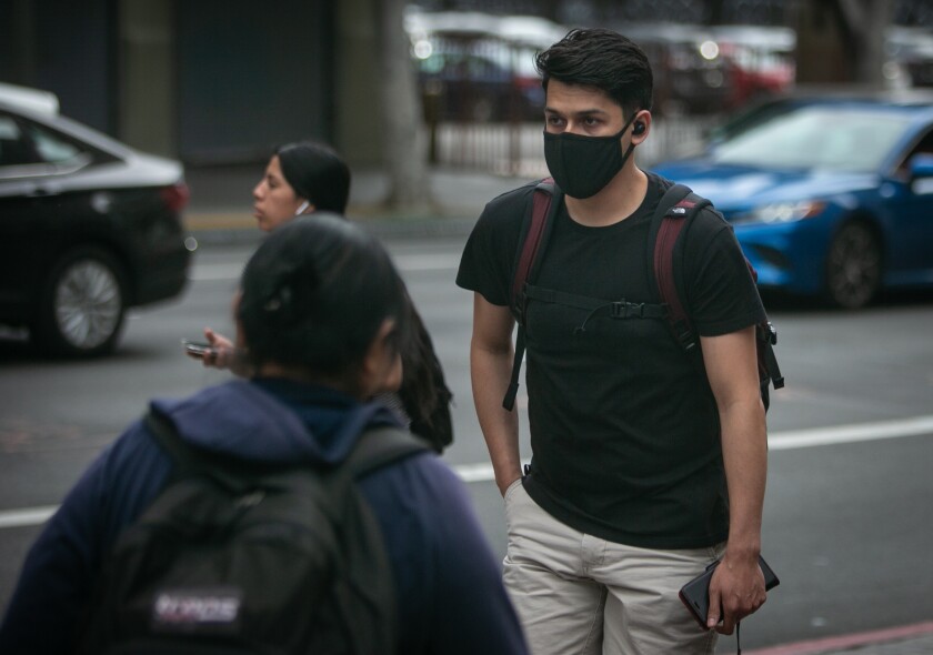 A man wearing a protective mask walks near the corner of 7th and Figueroa streets in Los Angeles on Thursday. 