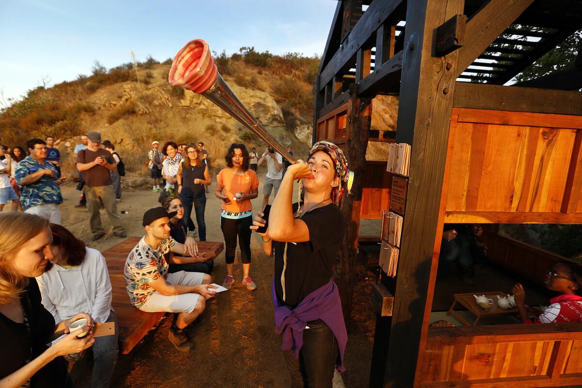 The Teafaerie blows her horn during sunrise as a group gathers around a teahouse that was surreptitiously built in Griffith Park by a collective of artists on Monday night.